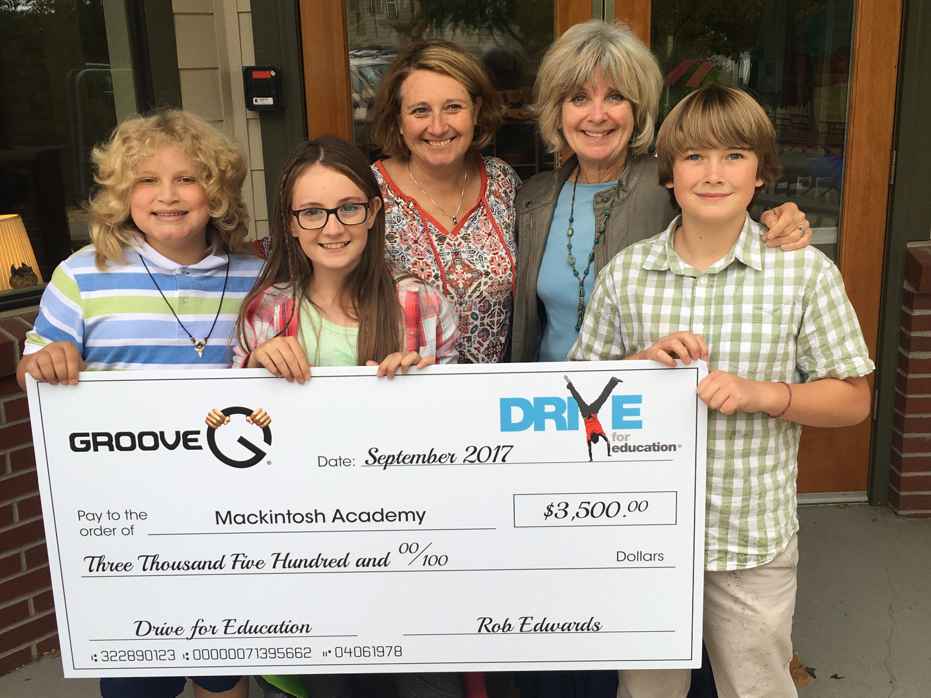 two adults and three students holding a giant award check from Groove Auto